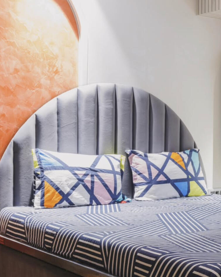 Modern bedroom interior featuring a grey velvet headboard and geometric print pillows in a Mumbai home.